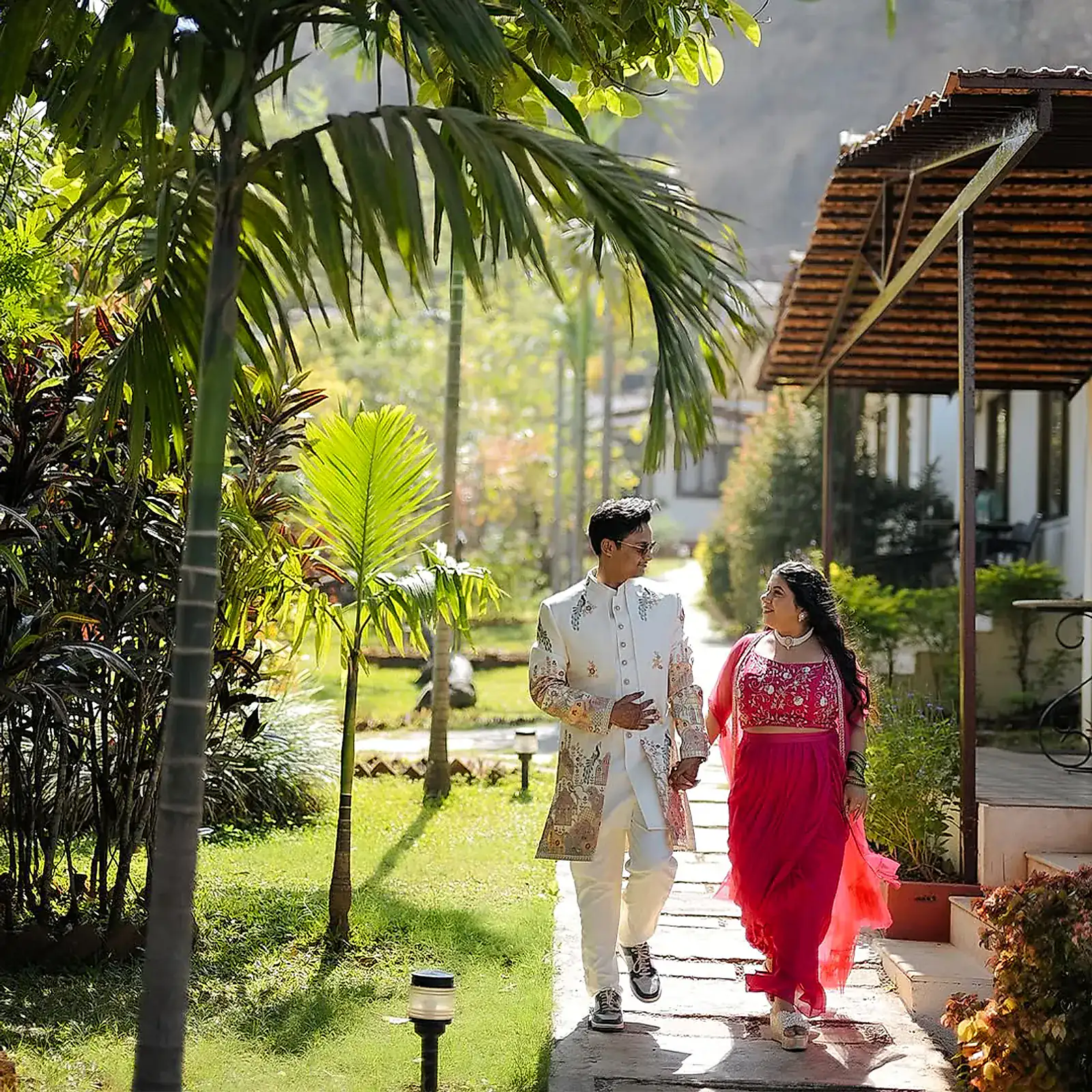 The couple walking hand in hand along a garden path between the cottages