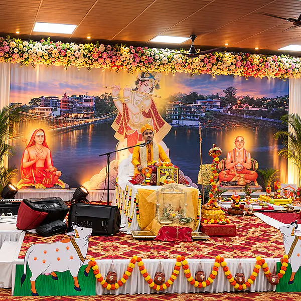 A stage decorated with marigolds and a Krishna backdrop, set for a spiritual discourse